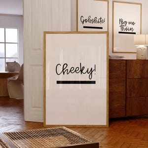 May include: Three framed prints with black calligraphy on a white background. The prints are hanging on a white wall. The prints say "Cheeky!" "Gobshite!" and "Póg mo thoin".