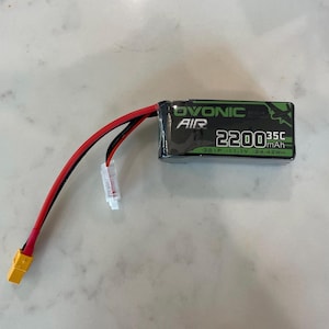 May include: A black and green battery pack with red and black wires and a yellow connector. The battery pack has the text "DVONIC AIR" and "2200mAh 35C".
