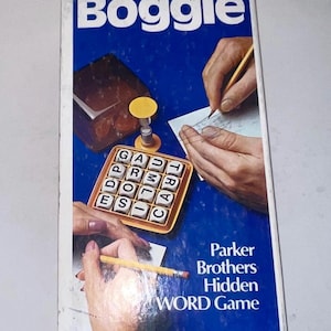 May include: Boggle word game box with a blue background. The box features the game's logo, a grid of lettered dice, and illustrations of hands playing. The text "Parker Brothers Hidden WORD Game" is also visible.