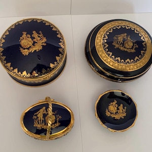 May include: Set of four blue and gold porcelain trinket boxes with a gold trim and a design of a couple in a garden. The boxes are in various sizes and shapes, including a round box, a square box, and an oval box with a handle.