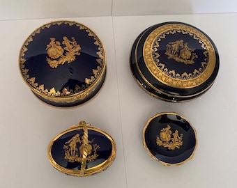 May include: Set of four blue and gold porcelain trinket boxes with a gold trim and a design of a couple in a garden. The boxes are in various sizes and shapes, including a round box, a square box, and an oval box with a handle.