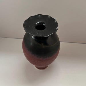 May include: A small, round, black and red ceramic vase with a flared, black rim.
