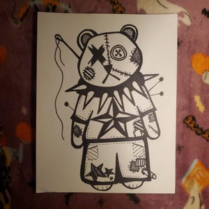 May include: Black and white illustration of a teddy bear with a stitched-up design. The bear has an X over one eye and a button on the other. It wears a star-shaped shirt and shorts with patches and pins.