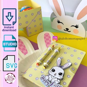 Puede incluir: Una tarjeta de Pascua de color amarillo y morado con un conejito blanco que sostiene una cesta. La tarjeta tiene un bolsillo para lápices de colores y dice "Feliz Pascua".