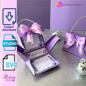 Puede incluir: Una caja de invitación de color lila claro con un lazo y asa a juego. La caja se abre para revelar tarjetas de invitación con diseños florales y texto. La imagen también muestra una segunda caja cerrada y bolas de discoteca.