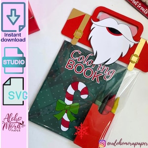 Puede incluir: Una bolsa de plástico transparente llena de un bastón de caramelo rojo y blanco, un libro para colorear verde con las palabras "Coloring Book" en la portada, un sobre rojo con un copo de nieve y un paquete de crayones. La bolsa está decorada con una maleta de Santa Claus roja y dorada y una barba de Santa Claus blanca.