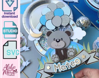 May include: A blue and gray cake topper featuring a teddy bear with a blue balloon, a crescent moon, and a banner that says "Mateo".