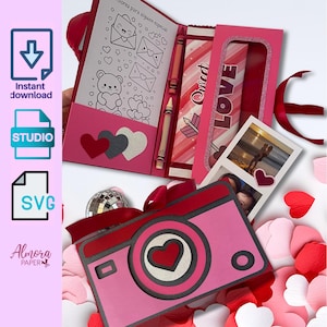 以下が含まれることがあります： 赤いハート型のレンズが付いたピンク色の紙製カメラ、塗り絵、そして「LOVE」という文字が入った箱。塗り絵にはテディベアとハートの絵が描かれています。箱にはカップルの写真が入っています。