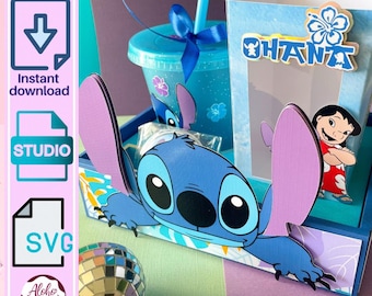 Op de afbeelding: Een blauw en paars papieren knutselwerk met het personage Stitch uit Lilo & Stitch. Het ontwerp omvat een beker, een popcornbox met het woord "OHANA" en een discobal. De afbeelding bevat ook de tekst "Direct downloaden", "STUDIO" en "SVG".