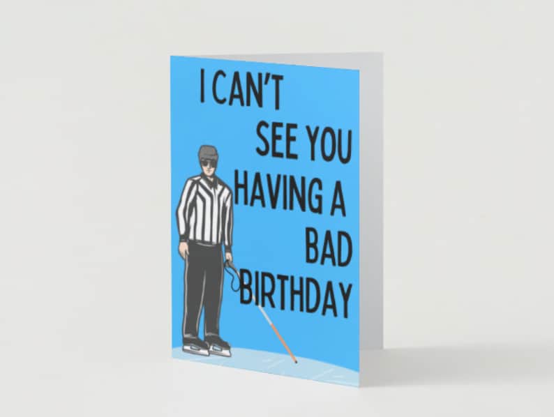 May include: A blue birthday card featuring a cartoon referee holding a white cane. The card reads "I can't see you having a bad birthday."