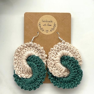 Può includere: Orecchini all'uncinetto con un design a spirale beige e verde. Gli orecchini sono fatti a mano e hanno un'etichetta che dice "fatto a mano con amore".