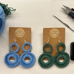Può includere: Due paia di orecchini all'uncinetto, un paio è blu e l'altro è verde. Gli orecchini sono cerchi a doppio strato con un cerchio più piccolo all'interno di un cerchio più grande. Gli orecchini sono fatti a mano e vengono forniti con una carta che dice "fatto a mano con amore".