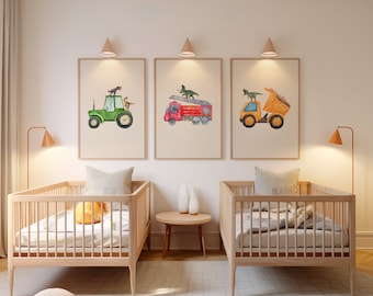 May include: Two wooden cribs with white mattresses and yellow pillows. Three framed prints on the wall above the cribs feature watercolor illustrations of a green tractor, a red fire truck, and a yellow dump truck, each with a dinosaur on top.