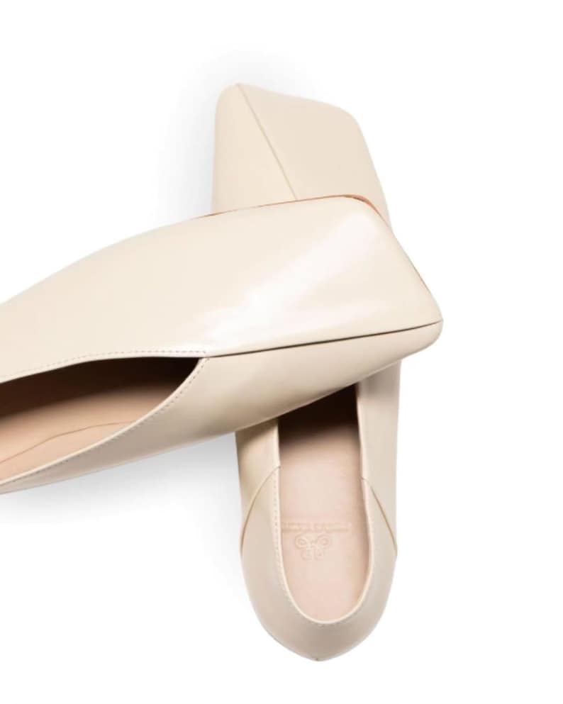 May include: Cream-colored leather flats with a unique, angular design. The shoes have a pointed toe and a low heel. The top-down view showcases the shoe's sleek silhouette and minimalist aesthetic. The flats are likely designed for comfort and style.
