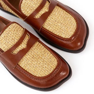May include: A pair of brown leather loafers with woven straw-colored panels. The shoes have a classic penny loafer design with a rounded toe and a dark brown sole. The shoes are displayed on a white background.