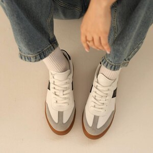 May include: White leather sneakers with black and gray accents and brown soles. The sneakers have a classic design with laces and a rounded toe.