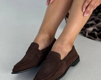 May include: Brown suede loafers with a classic design. These slip-on shoes feature a rounded toe and a low heel. The shoes are a rich, dark brown color, perfect for everyday wear.