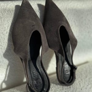 Könnte beinhalten: Ein Paar dunkelbraune Wildlederschuhe mit Absatz und einem Ausschnitt am Vorderblatt. Die Schuhe haben einen Slingback-Riemen und sind von der Marke "Jeffrey Campbell".