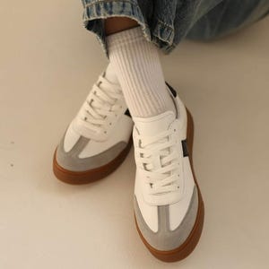 May include: White leather sneakers with a grey suede toe and a black stripe on the side. The sneakers have a gum sole.