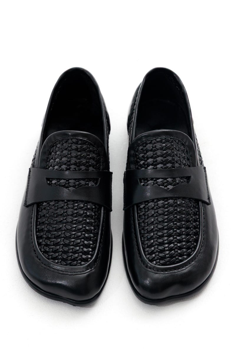 May include: A pair of black leather loafers. The shoes feature a woven design on the vamp and a strap across the top. The shoes are set against a white background.