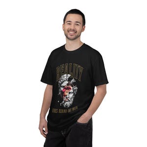 Peut inclure: Un t-shirt noir à manches courtes avec une impression graphique représentant un buste en pierre classique dont le visage de primate est visible à travers une fissure. Le texte REALITY est imprimé en doré au-dessus et HIDES BEHIND THE MASK en dessous.