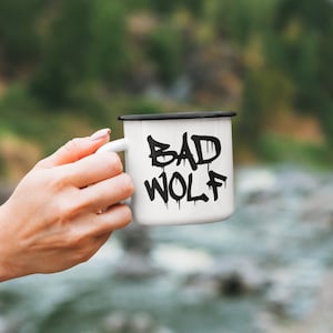 May include: White enamel mug with a black rim and a black graphic that says "BAD WOLF" in a dripping paint style.