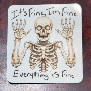 May include: A white square sticker with a black skeleton with raised arms and the text "It's Fine, I'm Fine Everything is Fine".