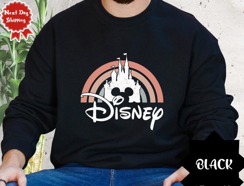 Puede incluir: Una sudadera negra de manga larga con un gr&aacute;fico blanco de la silueta de un castillo dentro de un arco&iacute;ris de tonos apagados. Debajo del castillo, la palabra Disney est&aacute; impresa en una fuente cursiva blanca. El dise&ntilde;o tiene una textura desgastada.