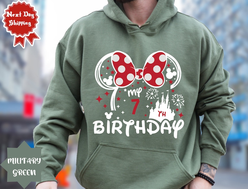 May include: Green hooded sweatshirt with a white graphic of Minnie Mouse ears, a bow, a castle, fireworks, and the text "My 7th Birthday".