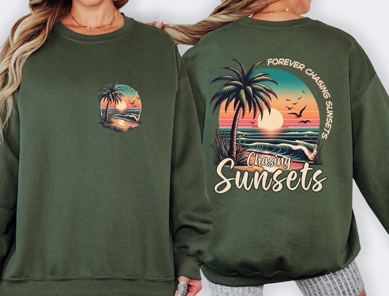 May include: Dark green sweatshirt featuring a sunset scene with palm trees, waves, and birds. The back of the sweatshirt has the text "Forever Chasing Sunsets" and "Chasing Sunsets" below the graphic.