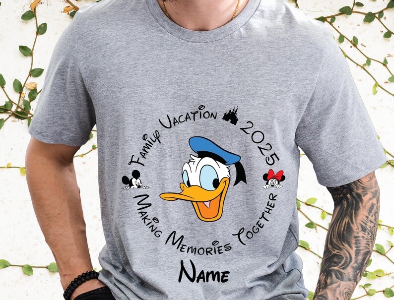 May include: Grey t-shirt with a circular design featuring Donald Duck in a blue sailor hat. The design includes the text "Family Vacation 2025 Making Memories Together" and a space for a name.