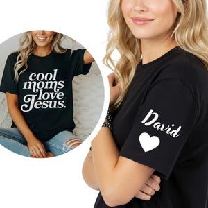May include: Black t-shirt with the text "cool moms love Jesus" in white script. The sleeve features the name "David" and a white heart. The shirt is a casual, everyday wear item.