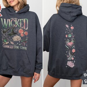 May include: Dark grey hooded sweatshirt with a graphic print of a witch's hat, stars, and the text "Wicked Changed For Good". The back of the sweatshirt has a vertical graphic print of a heart, stars, and a bird.