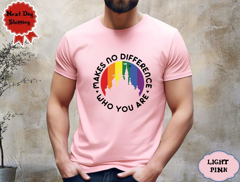 May include: A light pink t-shirt with a rainbow-colored circle featuring a silhouette of a castle and the text "It Makes No Difference Who You Are".