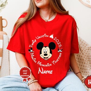 May include: A red t-shirt with a Mickey Mouse graphic. The design includes the text "Family Vacation 2025 Making Memories Together Name" in a circular arrangement around Mickey's face. A "Next Day Shipping" sticker is visible.