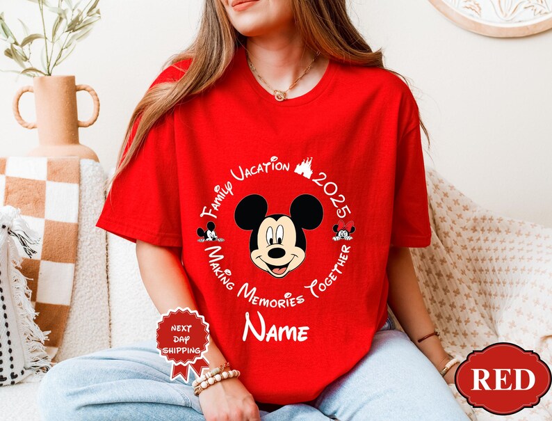 May include: A red t-shirt with a Mickey Mouse graphic. The design includes the text "Family Vacation 2025 Making Memories Together Name" in a circular arrangement around Mickey's face. A "Next Day Shipping" sticker is visible.
