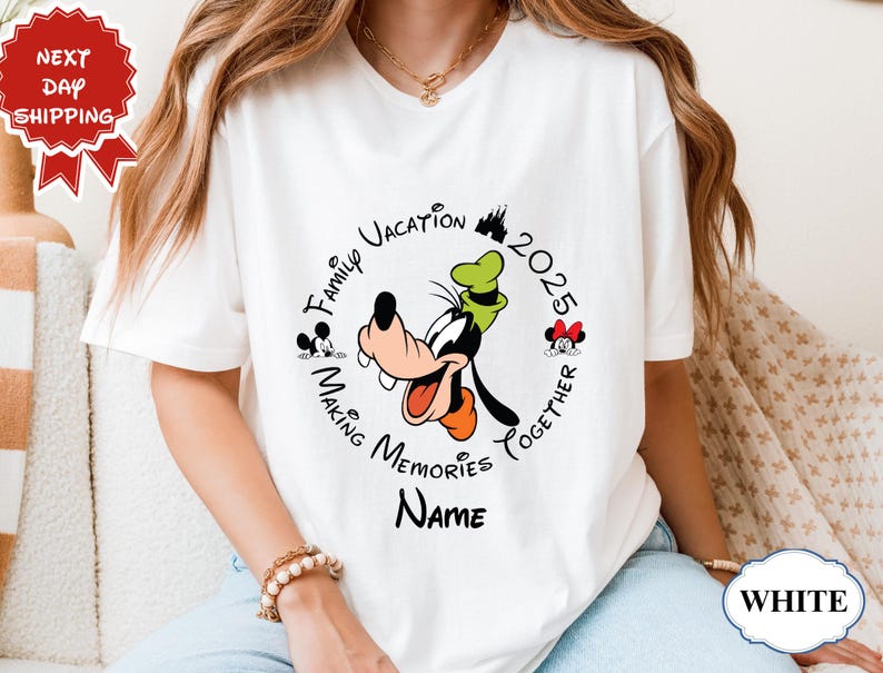 May include: White t-shirt with a circular design. The design includes the text "Family Vacation 2025 Making Memories Together" and cartoon images of Goofy, Mickey, and Minnie Mouse. The word "Name" is below the design.
