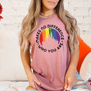 May include: A heather mauve t-shirt with a rainbow-colored circle around a silhouette of the Disney castle. The text inside the circle reads "Makes no difference who you are."