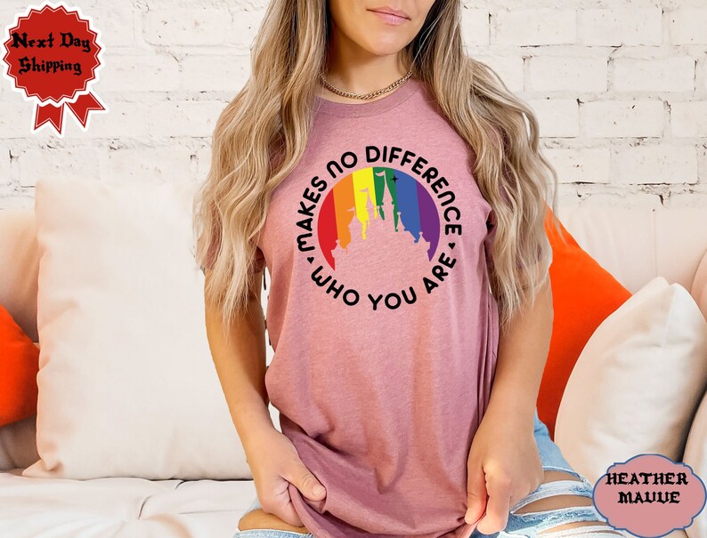 May include: A heather mauve t-shirt with a rainbow-colored circle around a silhouette of the Disney castle. The text inside the circle reads "Makes no difference who you are."