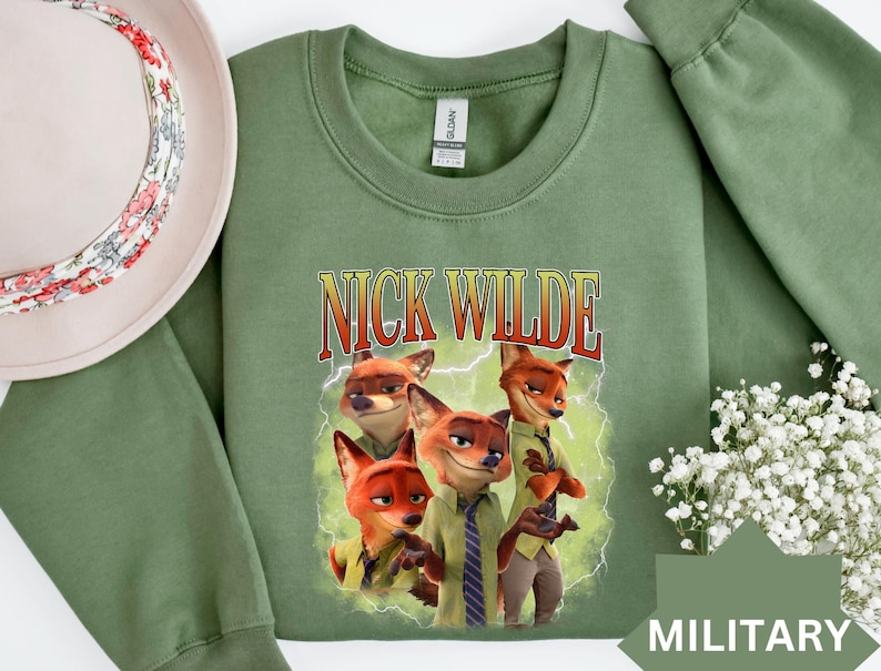 May include: A military green sweatshirt featuring a graphic of Nick Wilde from Zootopia. The design includes the text "NICK WILDE" in a vintage font, with illustrations of the character. The sweatshirt is a crew neck style.
