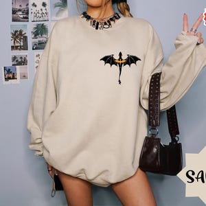 May include: A beige sweatshirt with a black dragon graphic on the front. The sweatshirt has a relaxed fit and is made of a soft, comfortable fabric.