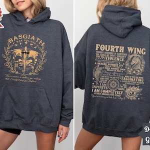 May include: Dark grey hooded sweatshirt with a gold graphic print on the front and back. The front graphic says "Basgiath War College" with a dragon design. The back graphic says "Fourth Wing" with a dragon design and text about violence and dragons.