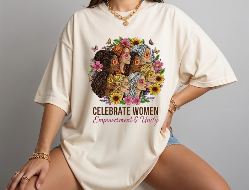 May include: Cream-colored t-shirt featuring a graphic of diverse women surrounded by flowers and butterflies. The text "CELEBRATE WOMEN Empowerment & Unity" is printed below the graphic. The shirt has short sleeves and a relaxed fit.