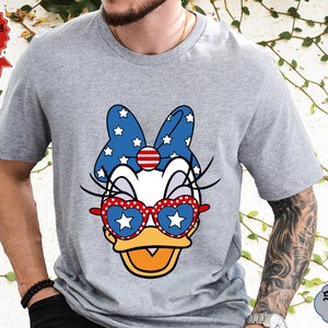 May include: A grey t-shirt with a cartoon image of a duck wearing red, white, and blue sunglasses and a bow with stars. The text "SPORT GREY" is visible in the bottom right corner of the image.