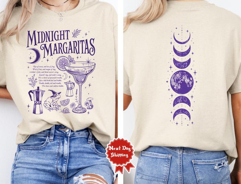 以下が含まれることがあります： 紫色のグラフィックプリントが施されたベージュのTシャツ。前面には「Midnight Margaritas」の文字、カクテルグラス、魔女の帽子をかぶったカエル、植物のイラストが描かれています。背面には月の満ち欠けが縦に並んでいます。