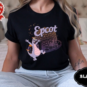 May include: Black t-shirt with a purple dragon and the text "Epcot" in white. The dragon is flying in front of a pink and purple Spaceship Earth.
