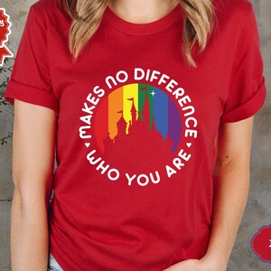 May include: Red t-shirt with a white circle graphic featuring a rainbow and a castle silhouette. The text inside the circle reads "Makes no difference who you are."