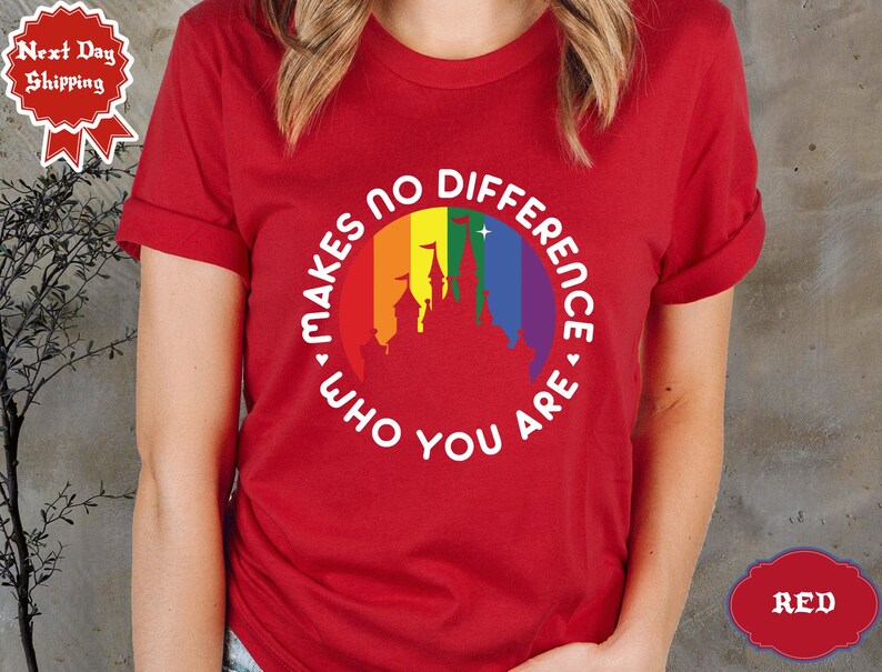 May include: Red t-shirt with a white circle graphic featuring a rainbow and a castle silhouette. The text inside the circle reads "Makes no difference who you are."