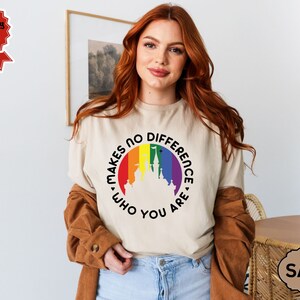 May include: A beige t-shirt with a rainbow-colored circle featuring a castle silhouette and the text "Makes No Difference Who You Are."