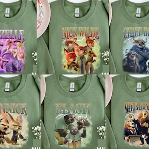 May include: Sage green sweatshirts featuring characters from the animated movie Zootopia. Each sweatshirt displays a different character's name and image: Gazelle, Nick Wilde, Chief Bogo, Finnick, Flash, and Mayor Lionheart. The designs are colorful and eye-catching.